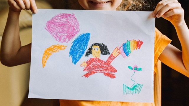 Flicka håller teckning med färgglada figurer framför ansiktet