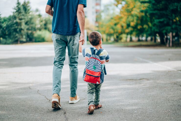 Pappa och barn håller varandra i handen och går över asfalterad gård