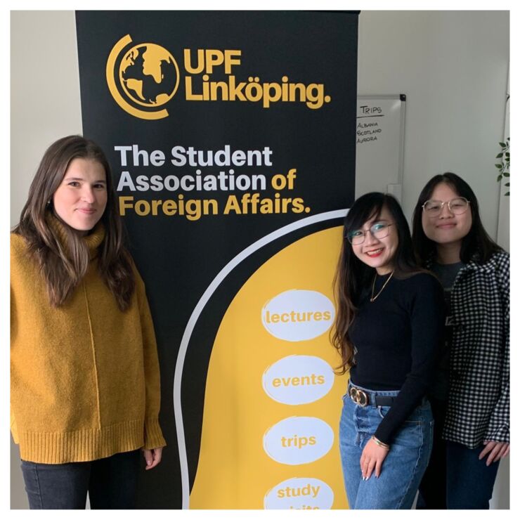 Episode guests Elyssa, Karolina and Vivian standing with a rollup with information about UPF Linköping.