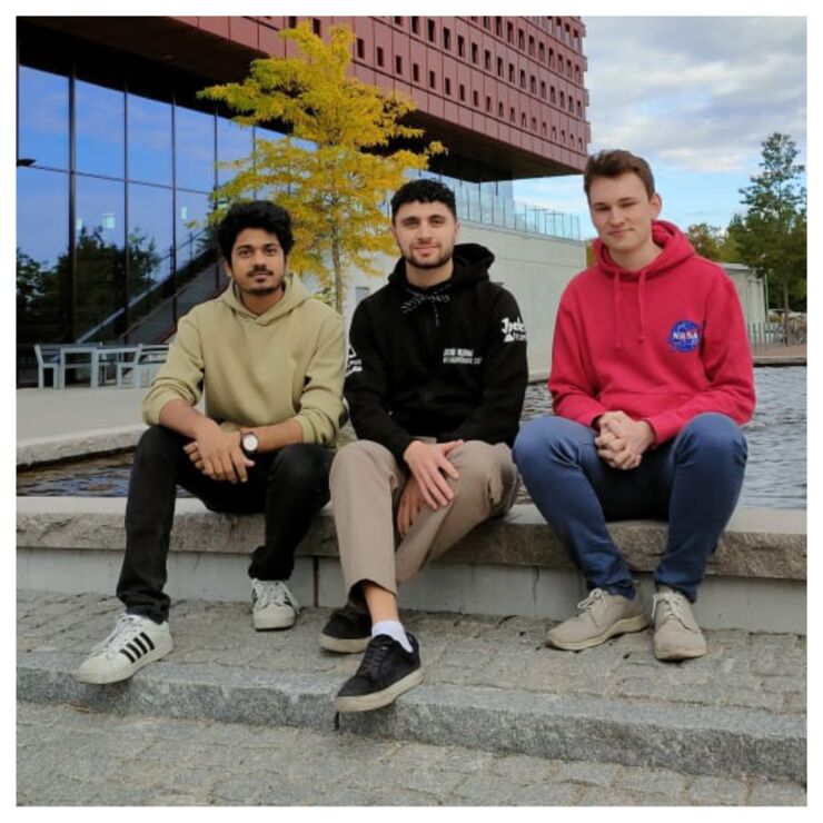 Three guys sitting outside Studenthuset at Campus Valla looking into the camera.