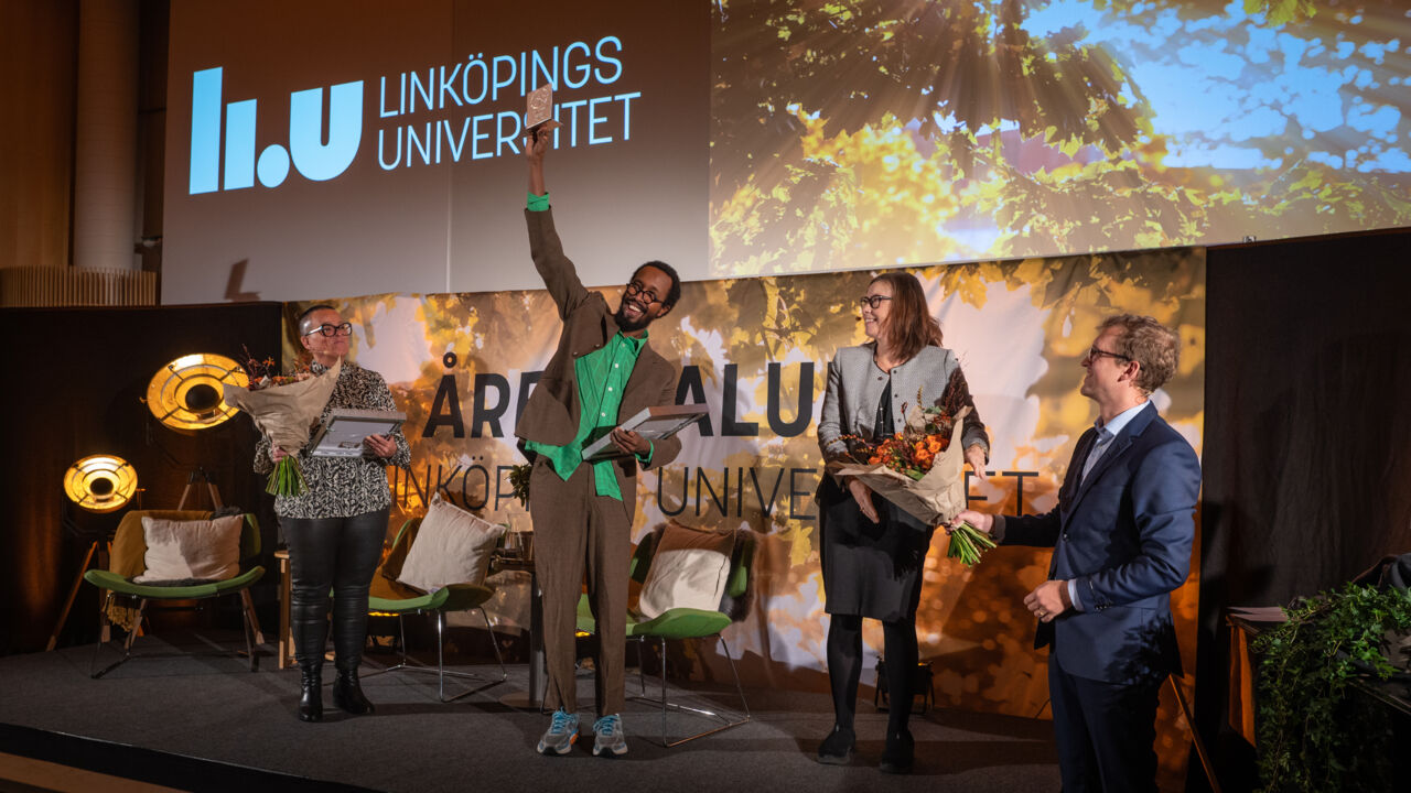 Glada människor på scen. I bakgrunden text 