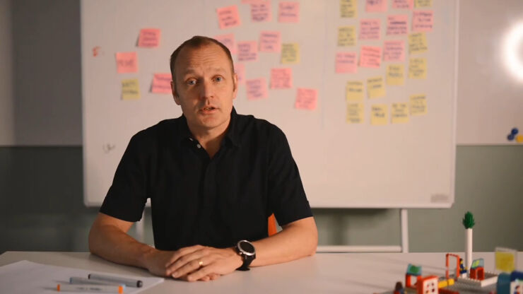 Man sitting at a desk with Lego, whiteboard with Post It notes in the background