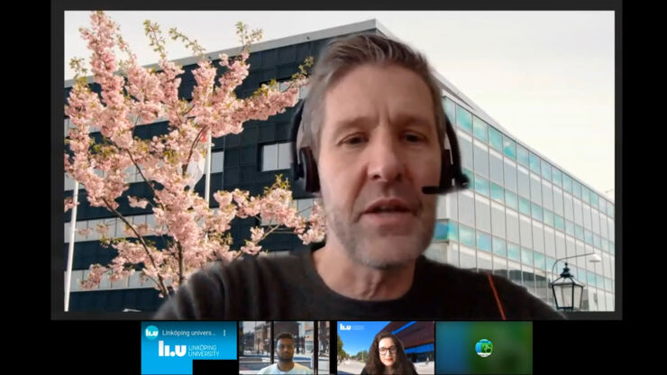 Man with stubble and headset in online meeting with house and flowering tree in the background