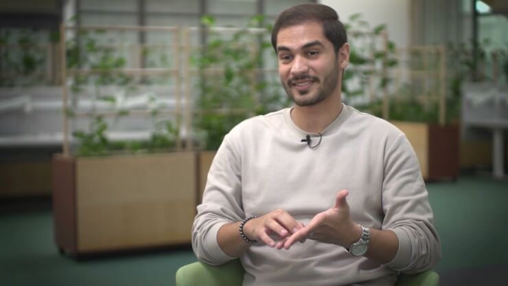 Young man in beige sweater with green plants in the background