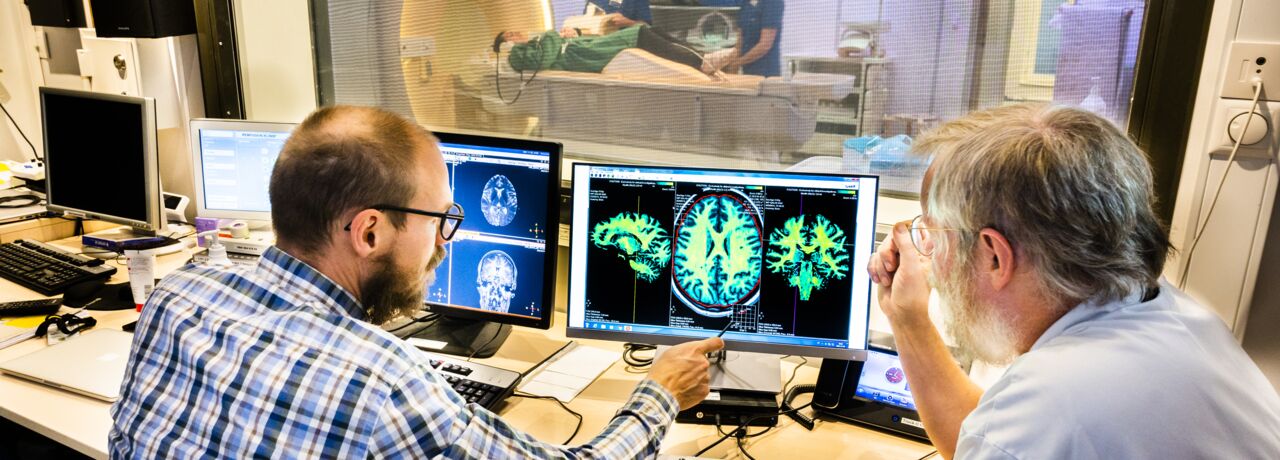 Anders Tisell and Peter Lundberg in front of the MR scanner looking at brain images.