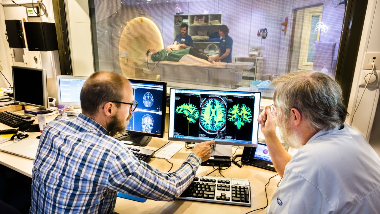 Anders Tisell and Peter Lundberg in front of the MR scanner looking at brain images.