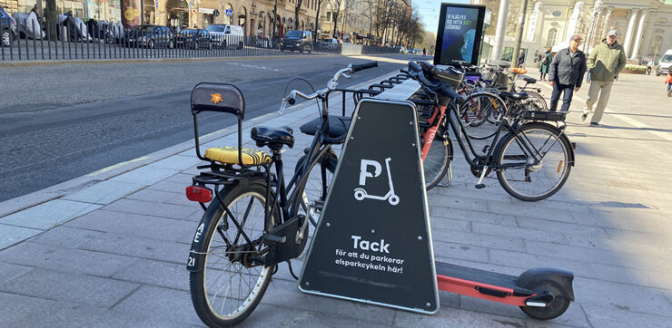 En parkeringsplats för elsparkcyklar bredvid ett cykelställ i en trafikerad stadsdel.