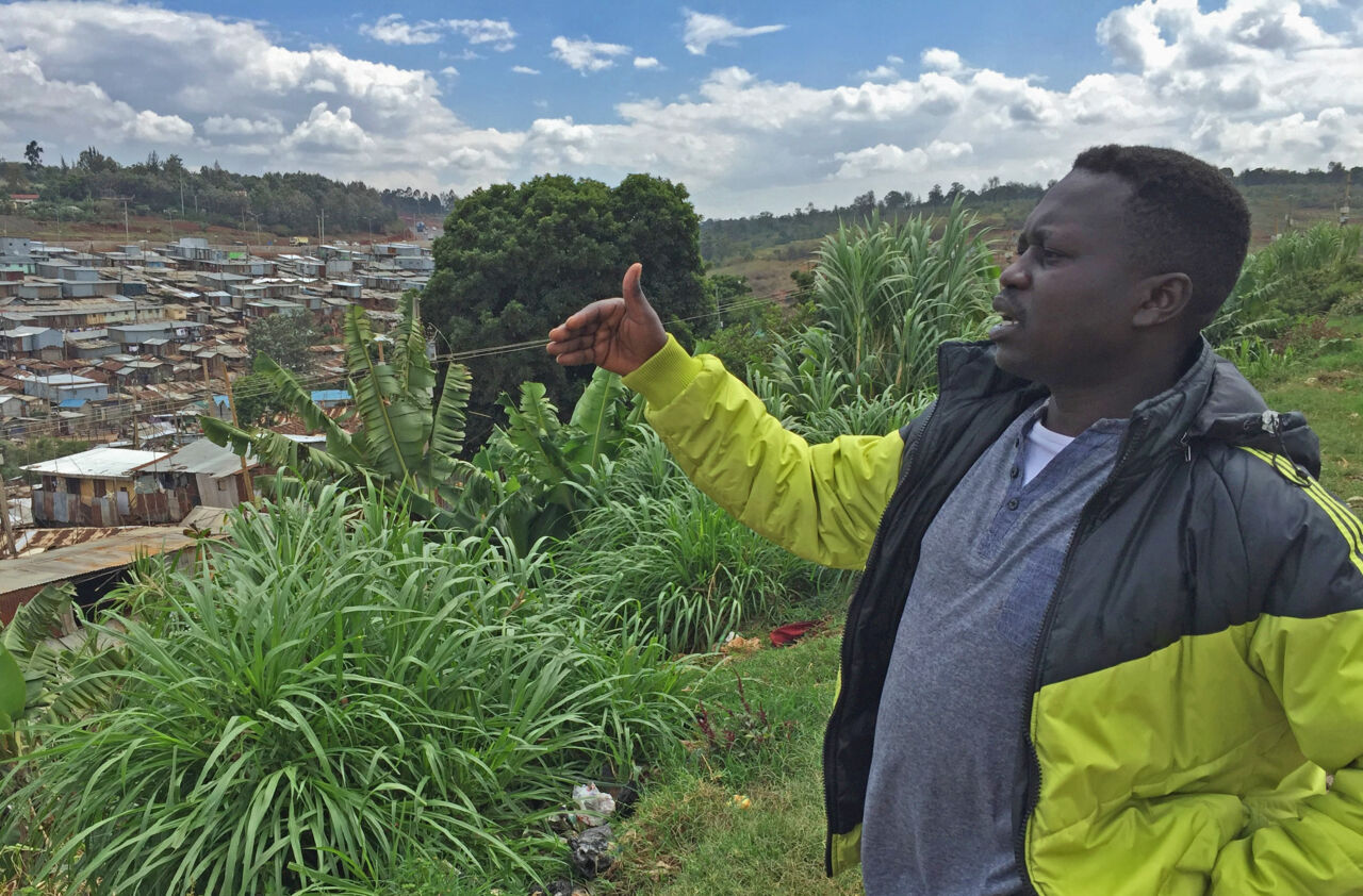 Afrikansk man står på en höjd och blickar ut över en stad.