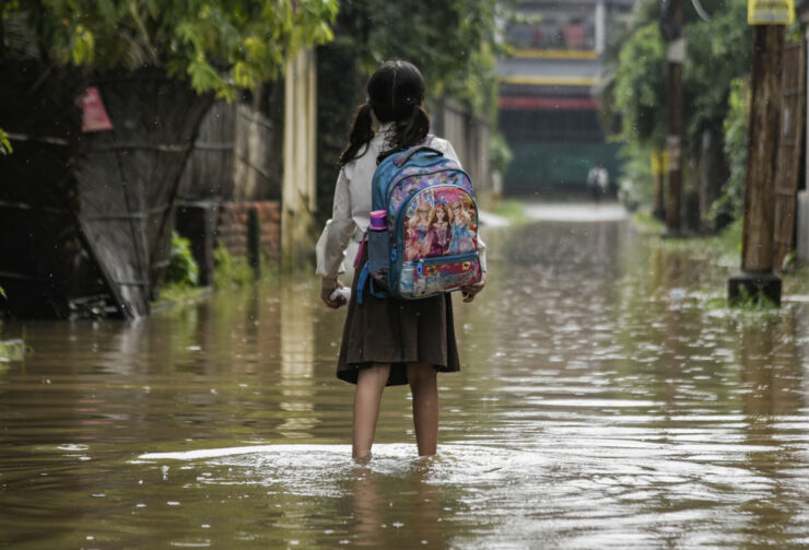 Flicka med ryggsäck står i översvämmad stadsmiljö.