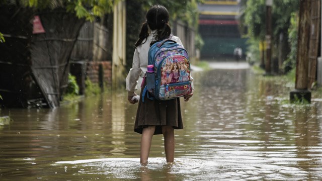 Flicka med ryggsäck står i översvämmad stadsmiljö.