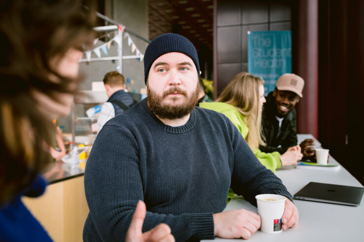 Manlig student med mössa i samtal med en studiekamrat.