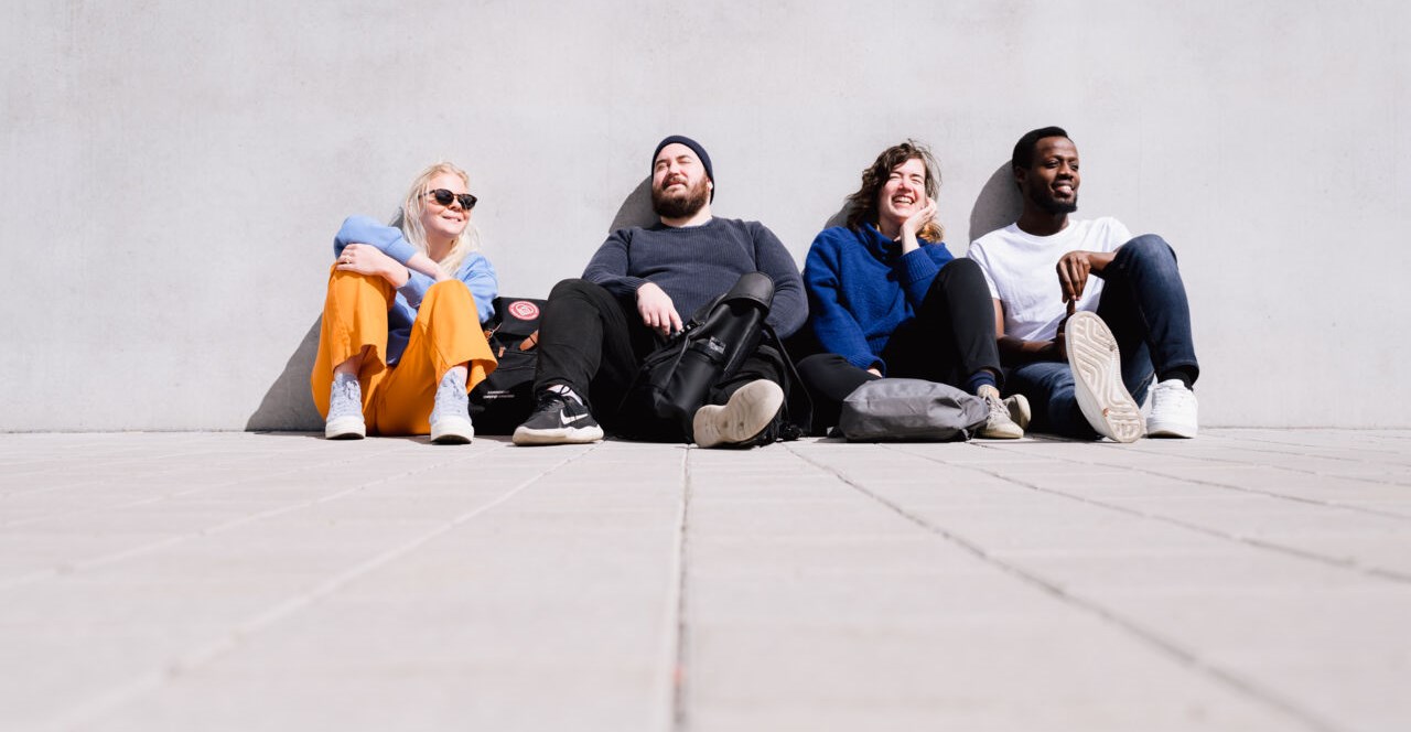 Fyra personer sitter lutade mot en vägg utomhus
