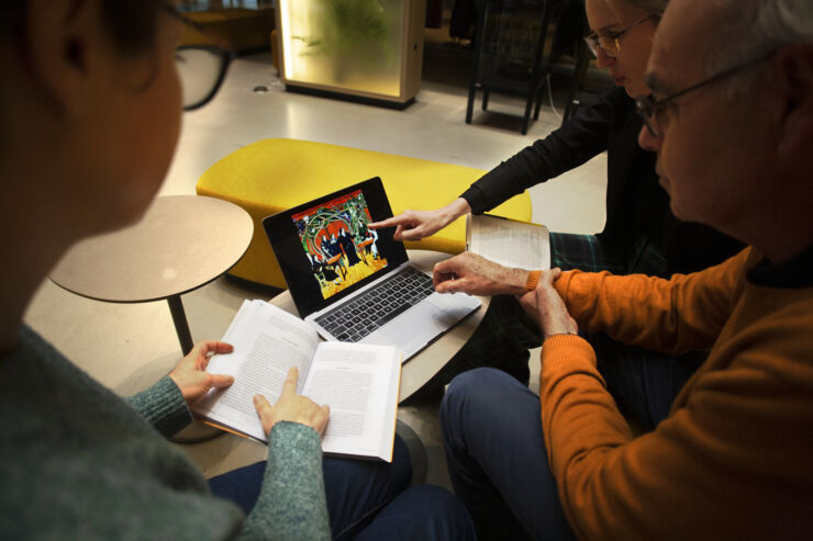 Tre personer diskuterar innehåll från uppslagna böcker och en laptop.