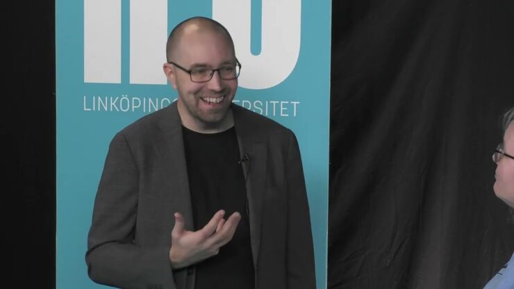 Smiling and gesticulating man in front of blue rollup