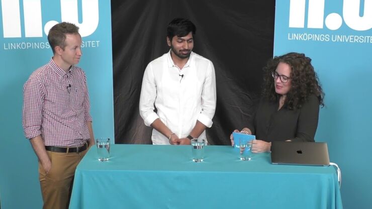 Two men and one woman standing at a table with blue tablecloth