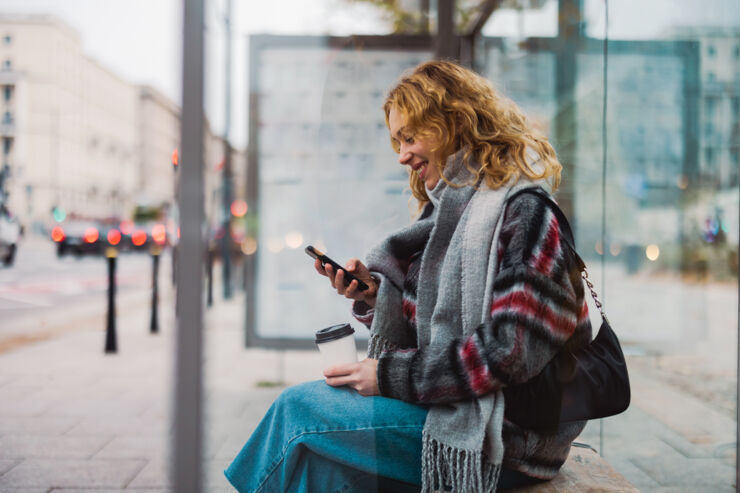 Kvinna sitter med sin smartphone vid en busshållplats.