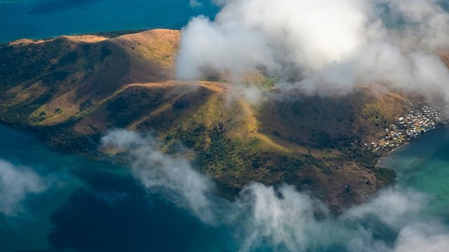 An island in the Pacific Ocean with clouds all around seen from above.