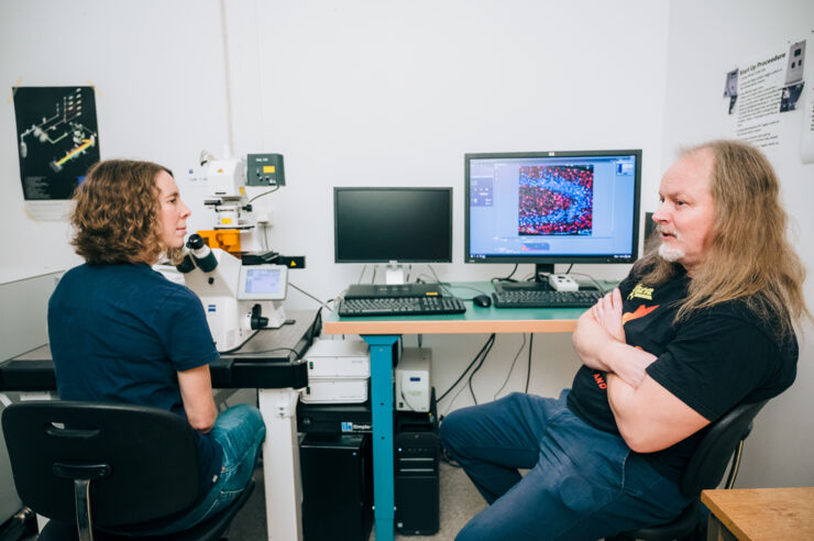 Two researchers by a microscope and a computer screen.