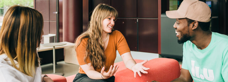 Three students sitting in a red sofa conversating