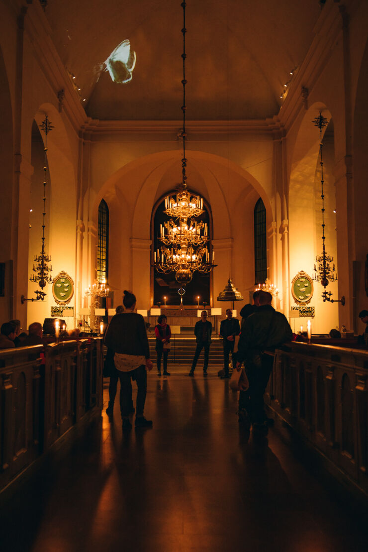 Bild inifrån en kyrka dovt upplyst av ljus. I taket syns en projektion av en fjäril.