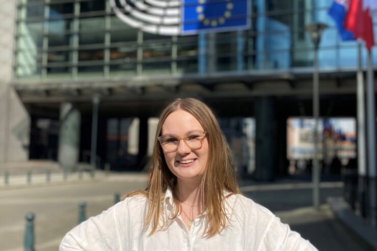 Ung kvinna i glasögon ståendes framför byggnad med EU-flagga