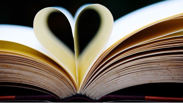 A book that is open, one of the pages has been shaped into a heart.