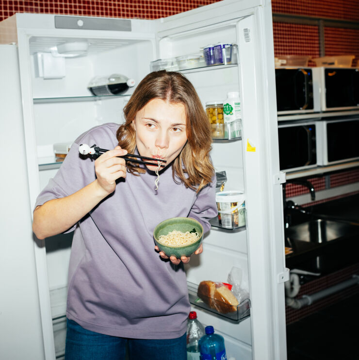 Kvinnlig student som äter nudlar vid ett öppet kylskåt