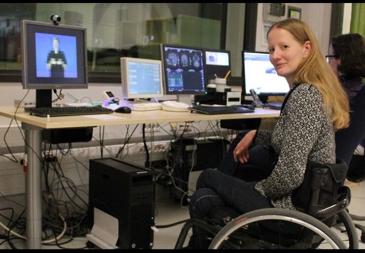 Kvinna i rullstol sitter i ett rum med datorskärmar.