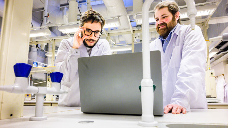 Two men in white lab coats with a computer in a lab.