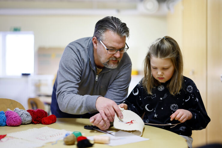 En manlig fritidshemslärare hjälper ett barn som broderar.