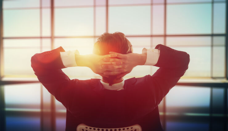 Man in office with hand behind his head.