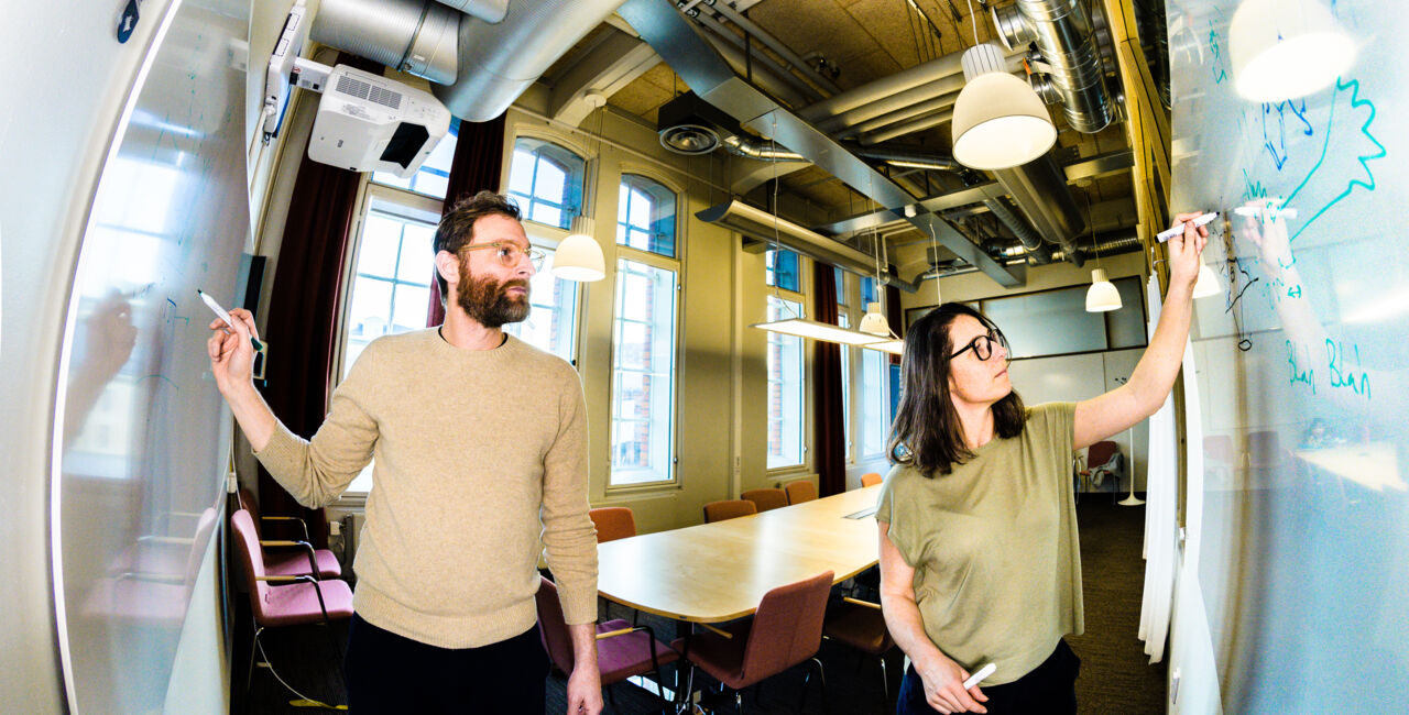 Two persons drawing on a whitboard.