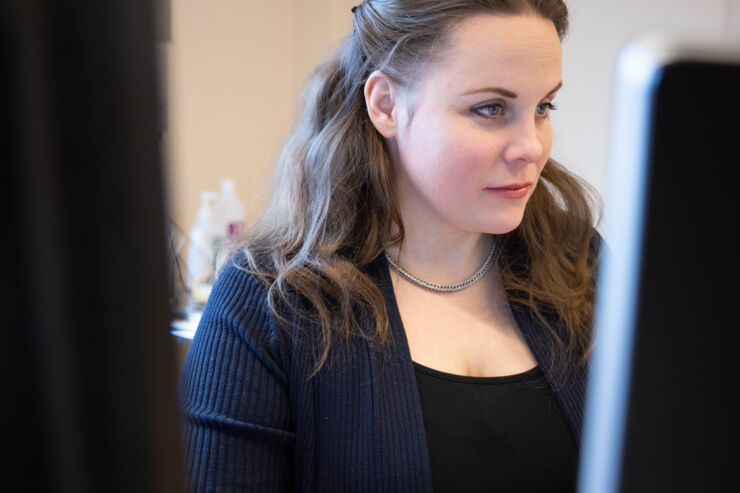 Woman sits in front of two computer screens and works.