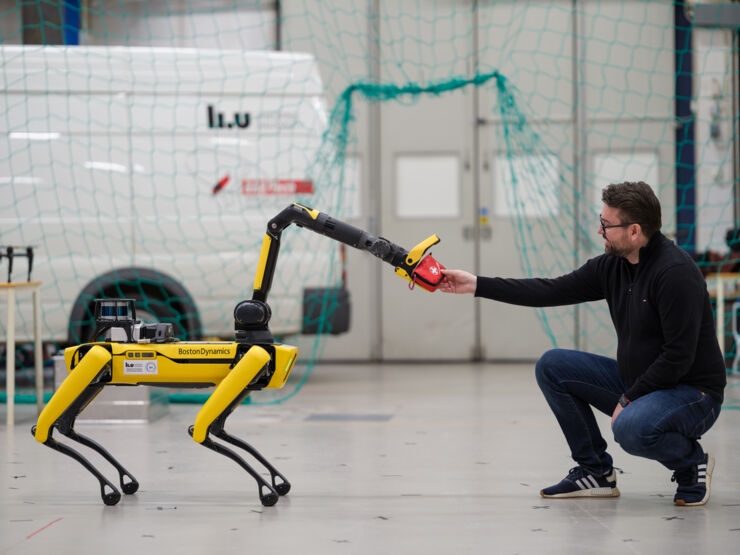 The robotdog Spot hands over a first aid kit to a kneeling man