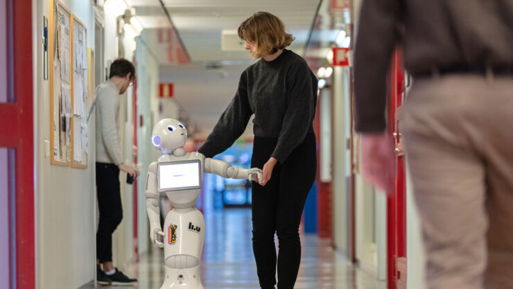 A woman is walking in a corridor together with a service robot 