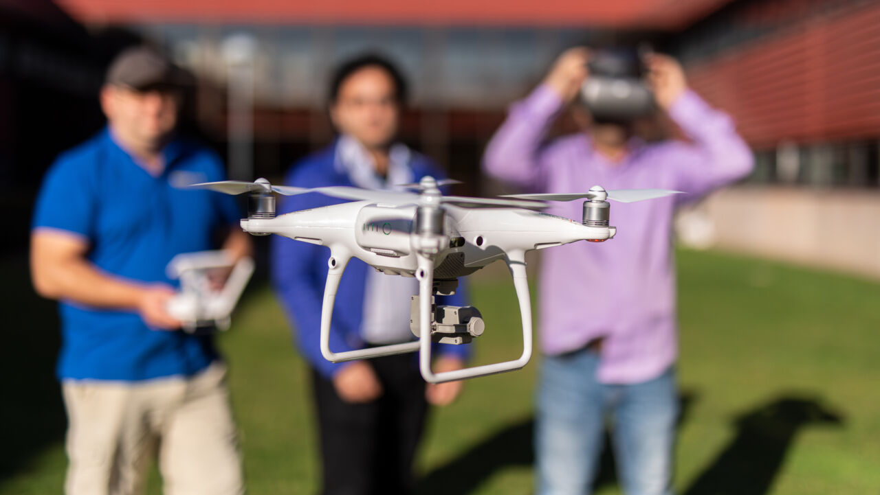 Drone in the air with three people in the background.