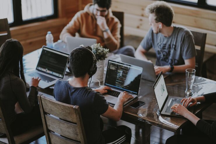 A group of  people sitting around table and working with computer.