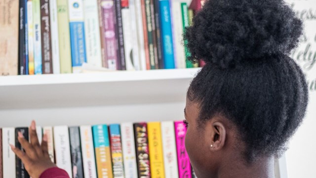 Girl in front of a bookshelf reaching for books.