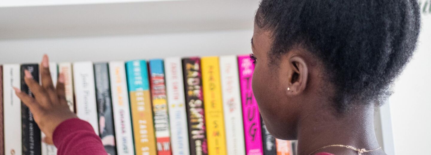 Girl in front of a bookshelf reaching for books.