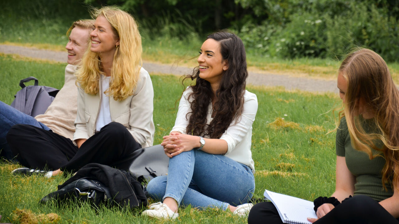 Studenter sitter på gräsmatta.