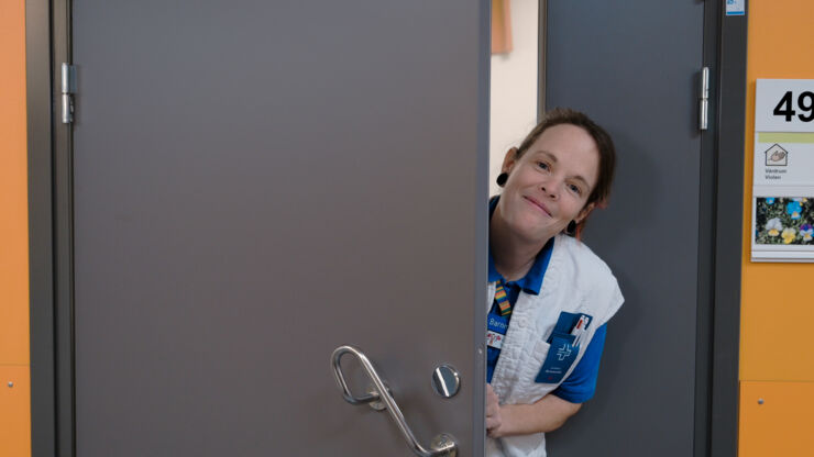 Kvinna i sjuksköterskekläder kikar ut genom dörr