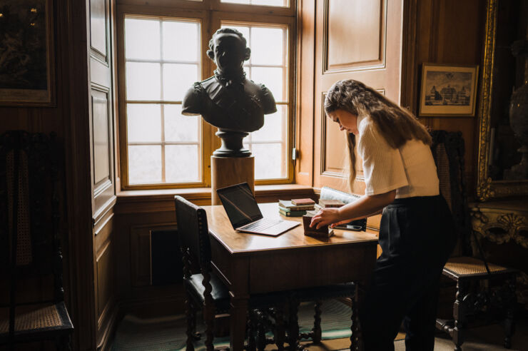 Woman standing by an old table covered in books.