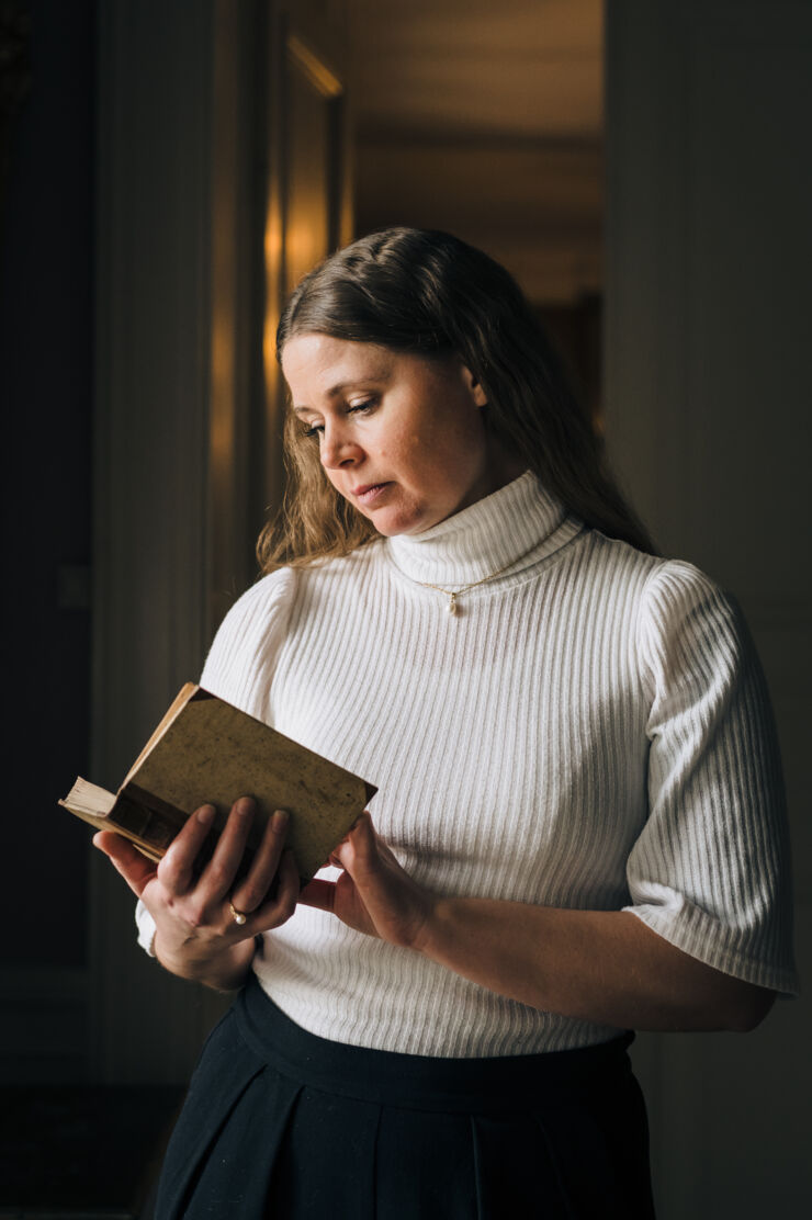 Woman in a white blouse holding a book.