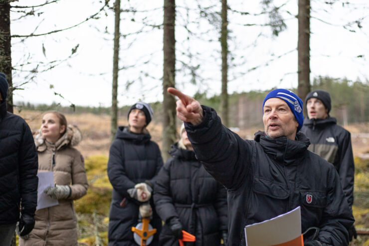 En person står och pekar ute i skogen med en lyssnande publik.