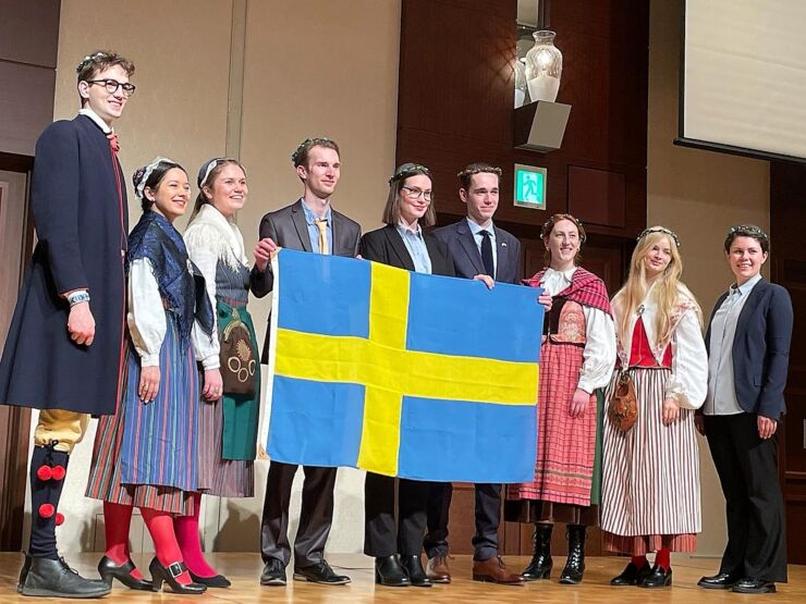 Grupp av unga människor i svenska nationaldräkter, håller i svenska fflagga. 