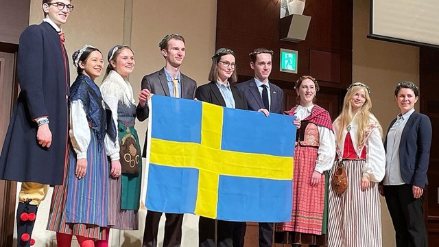 A group of young people in the Swedish nationl costumes holding the Swedish flag.