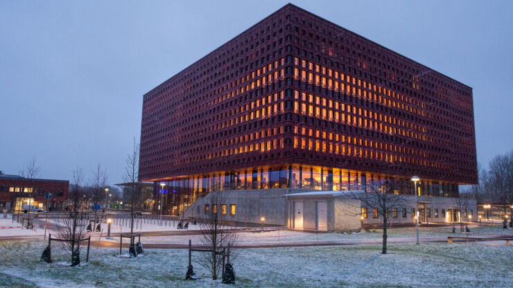 En stor byggnad i skymningsljus, det lyser i fönstren, på marken utanför finns lite snö.