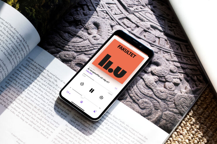 Mobiltelefon ligger på ett bord och visar podden Fakultet på skärmen.