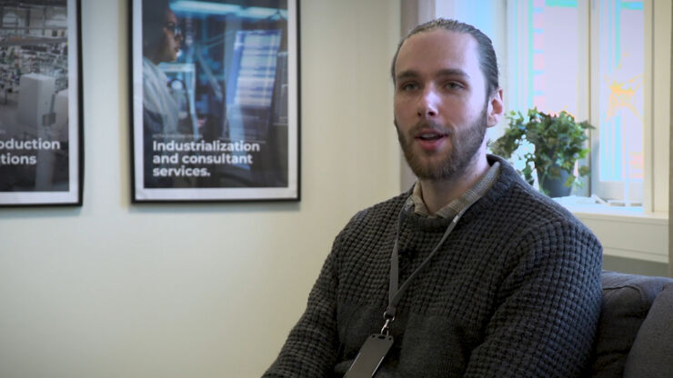 Ung man med kort i snöre runt halsen sitter framför fönster