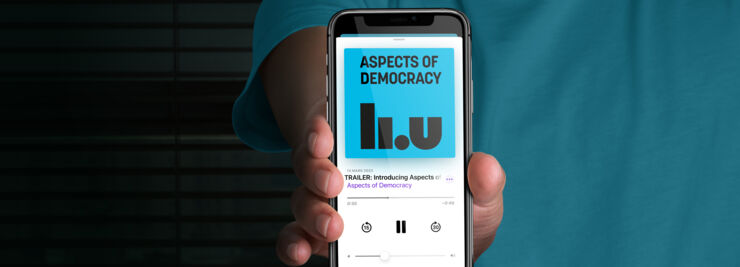 Person holding up smartphone with the podcast Aspects of Democracy on the screen.